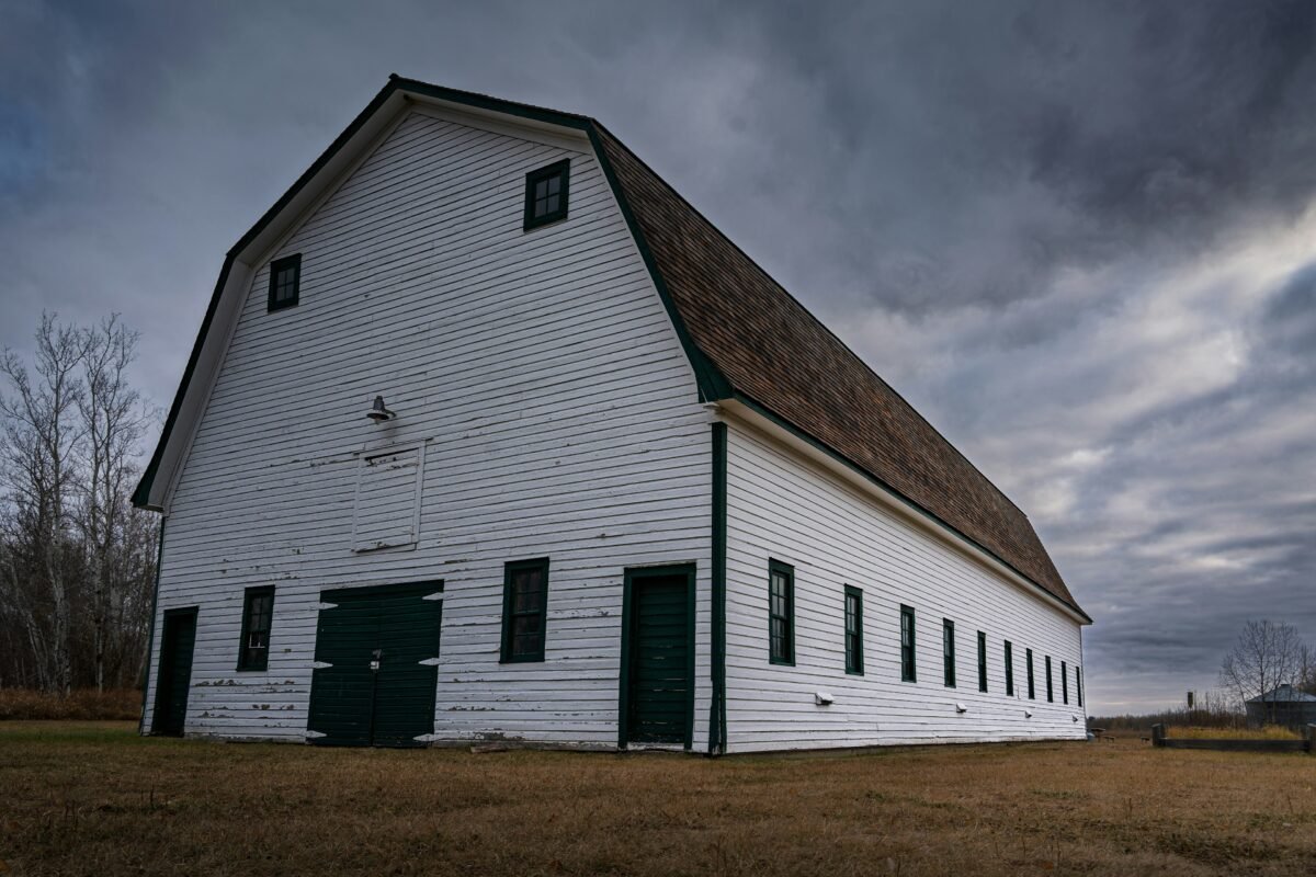 White barn with green doors in an autumn field under a dramatic sky